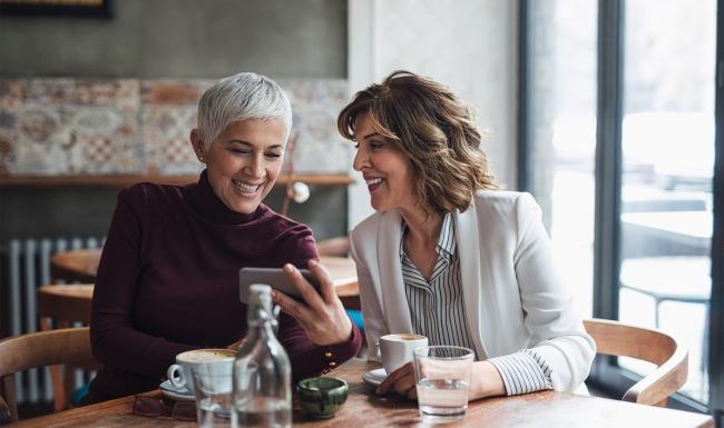two women sitting at a table looking at a phone